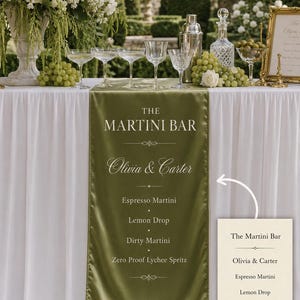 May include: An olive green satin table runner featuring white printed text that reads The Martini Bar, Olivia & Carter, and a list of drinks including Espresso Martini, Lemon Drop, Dirty Martini, and Zero Proof Lychee Spritz with decorative lines.