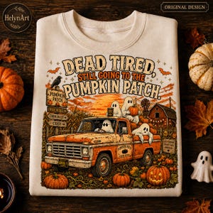 Op de afbeelding: Een beige sweater met ronde hals en een afbeelding van een oranje pick-up truck bestuurd door geesten, met de tekst "DEAD TIRED STILL GOING TO THE PUMPKIN PATCH". Het ontwerp bevat pompoenen, een schuur, een kraai en een houten wegwijzer.