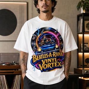 May include: A white short-sleeve t-shirt featuring a graphic of a blue car with four figures inside, surrounded by a vinyl record, musical notes, and lightning. The text reads BEATLES-A-RAMA VINYL VORTEX in yellow and blue lettering.