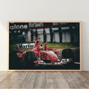 Könnte beinhalten: Ein gerahmter Fotodruck eines roten Formel-1-Rennwagens mit dem Fahrer im Cockpit, der beide Hände jubelnd in die Luft streckt. Das Auto zeigt deutliche Marlboro- und Vodafone-Schriftzüge, schwarze Reifen und ein aerodynamisches Karosseriedesign.