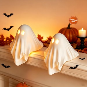 May include: Two white ghost-shaped lamps with glowing yellow oval eyes. The figures have a draped, fabric-like appearance with soft folds. Each lamp emits a warm light from within, creating a soft illumination against the surrounding space.