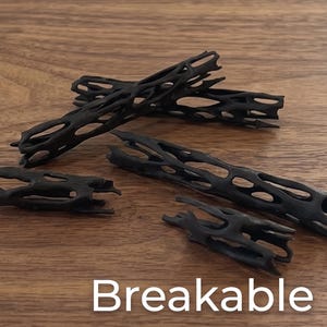 May include: Four black, cylindrical, hollow objects with an intricate, lattice-like, open-work structure. The pieces vary in length and thickness, featuring irregular, elongated openings throughout their surfaces. The word Breakable is printed below.