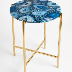 May include: A round side table featuring a tabletop composed of polished blue agate slices with varied concentric patterns. The table is supported by a slender, metallic gold-finished frame with four straight legs connected by a central cross-brace.