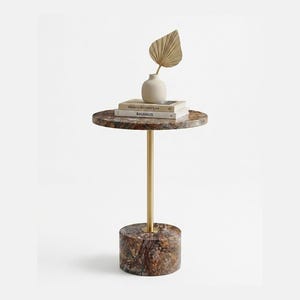 Op de afbeelding: Een ronde bijzettafel met een blad en voet van bruin en zwart gemarmerde steen, verbonden door een dunne goudkleurige metalen stang. Op de tafel liggen twee op elkaar gestapelde boeken met de titels Modern Architecture en BAUHAUS met een vaas.