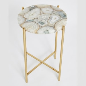 May include: A round side table featuring a tabletop composed of polished, multi-tonal white and grey agate slices. The table is supported by a slender, gold-finished metal frame with four straight legs connected by a central X-shaped crossbar.