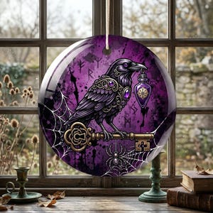 May include: A circular hanging ornament featuring a black raven perched on an ornate gold key. The background is a deep purple with a white spiderweb, a small spider, and faint runic symbols. The raven holds a purple potion bottle in its beak.
