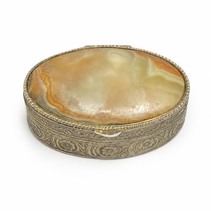 May include: An oval trinket box featuring a polished, multi-coloured agate stone lid with swirling bands of amber, cream, and green. The base is crafted from ornate, silver-toned metal with embossed floral patterns and a beaded edge trim.