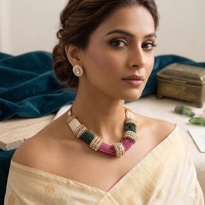 May include: A multi-strand beaded necklace featuring alternating segments of white, green, and pink seed beads, accented with gold-toned cylindrical spacers set with clear stones. Matching oval-shaped stud earrings with clear stones are worn.