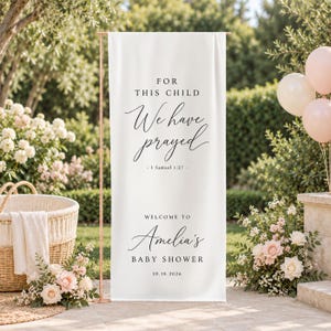 Op de afbeelding: Een hoog, rechthoekig wit verticaal spandoek met zwarte tekst: FOR THIS CHILD We have prayed - 1 Samuel 1:27 - WELCOME TO Amelia's BABY SHOWER 10.18.2026. Het spandoek is bevestigd aan een dunne, koperkleurige metalen standaard.