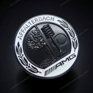 Könnte beinhalten: Ein kreisförmiges schwarz-weißes Emblem mit dem Schriftzug AFFALTERBACH oben und AMG unten. Das Design zeigt einen stilisierten Baum auf der linken Seite und ein Ventilfeder-Element auf der rechten Seite, eingerahmt von weizenartigen Ähren.