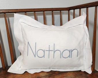 May include: White pillow with a gray embroidered name "Nathan" on a wooden chair.
