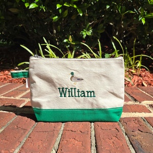 May include: A white canvas zippered pouch with a green bottom. The pouch has an embroidered green duck and the name "William" in green thread.