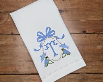 May include: White kitchen towel with a blue embroidered monogram and two frogs holding umbrellas.