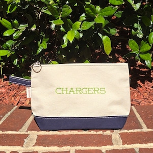 May include: A cream-colored canvas zippered pouch with a navy blue bottom. The pouch has a green embroidered word "CHARGERS" on the front.