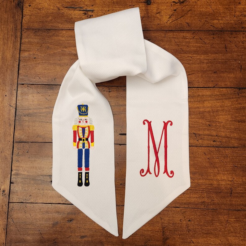 May include: White fabric Christmas stocking with a red and blue embroidered nutcracker and the letter "M" in red.