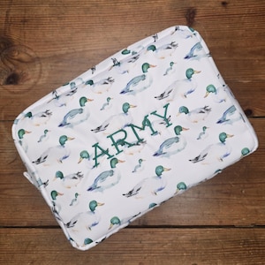 May include: White rectangular cosmetic bag with a pattern of watercolor ducks in shades of blue, green, and white. The word "ARMY" is embroidered in green on the front of the bag. The bag is closed with a zipper.