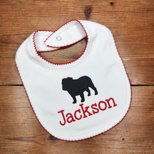 May include: White baby bib with red trim and a blue bulldog silhouette. The name "Jackson" is embroidered in red below the bulldog.