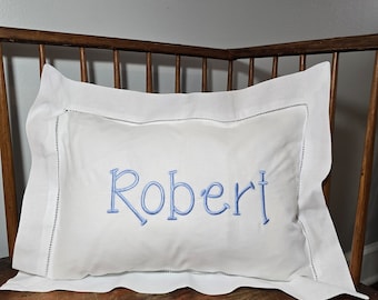 May include: White pillow with a blue embroidered name "Robert" on a wooden bench.