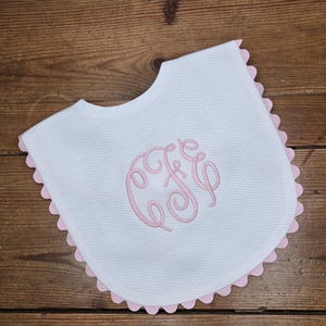 May include: White baby bib with a pink scalloped edge and a pink embroidered monogram "C&C".