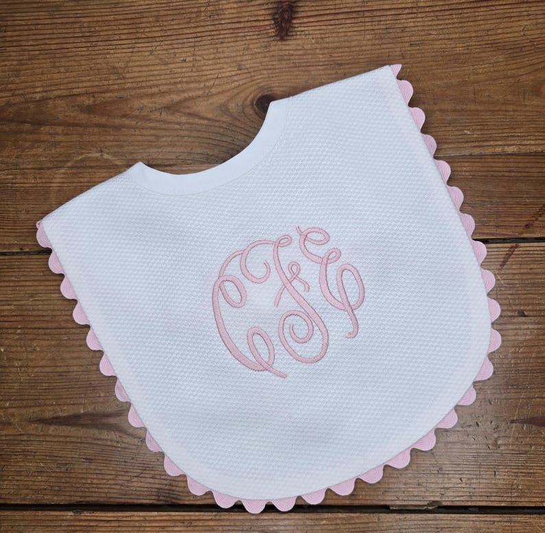 May include: White baby bib with a pink scalloped edge and a pink embroidered monogram "C&C".