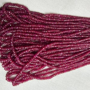 Può includere: Un lungo filo di piccole perline di rubino rosso scuro sfaccettate, disposte in diverse file parallele. Ogni singola perlina presenta una forma circolare con una superficie tagliata e riflettente che cattura la luce, creando un aspetto uniforme.