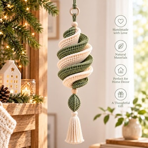 May include: A hanging spiral ornament crafted from sage green and cream-colored yarn. The structure features a twisted, ribbed design suspended by a cord with a wooden bead, ending in a smaller green crocheted sphere and a cream-colored tassel.