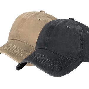 May include: Two baseball caps, one in a tan color and one in a black color. Both caps feature a six-panel construction with a curved brim, stitched detailing on the visor, and a small button at the top center of the crown. The fabric has a washed finish.