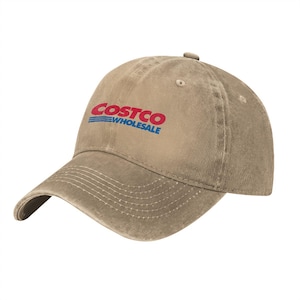 May include: A tan baseball cap with a distressed, washed-out texture. The front features the red and blue Costco Wholesale logo embroidered in a bold font. The cap has a curved brim with visible stitching and a button on the top crown.