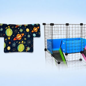 May include: A dark blue fabric mat featuring a colorful space pattern with planets, rings, and stars, positioned next to a black wire grid enclosure with blue plastic panels, a green ramp, and a pink ramp for small animal housing.