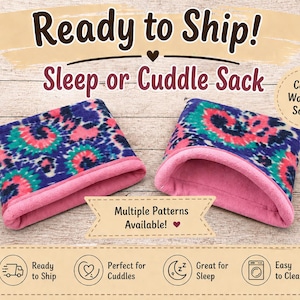May include: Two fleece sleep or cuddle sacks. Each has a tie-dye pattern in blue, pink, and teal, with a pink interior and trim. The image includes text that says "Ready to Ship!" and "Multiple Patterns Available!"