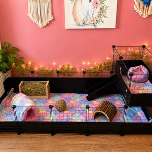 May include: A black wire pet cage with a multi-level design, featuring a ramp, a loft, and a colorful galaxy-patterned floor liner. The enclosure includes a wooden hay rack, a woven ball, a wooden tunnel, and a plush tie-dye bed.