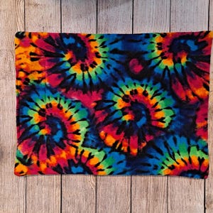 Może przedstawiać: Prostokątny kawałek materiału z żywym wzorem tie-dye, przedstawiający wirujące motywy w jasnych odcieniach niebieskiego, zielonego, ż&oacute;łtego, pomarańczowego i r&oacute;żowego na ciemnym tle. Tkanina posiada widoczne linie przeszyć biegnące pionowo.