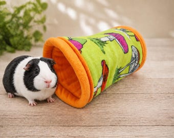 May include: A black and white guinea pig stands next to a cylindrical fabric tunnel. The tunnel features a bright lime green exterior with a colorful mushroom pattern and a solid orange fleece lining at both ends of the tube structure.