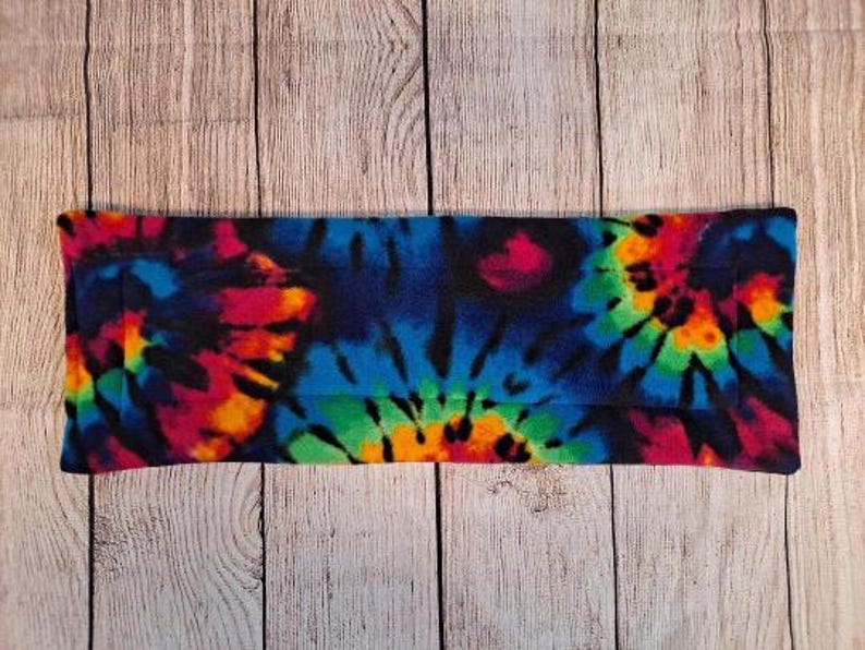 Może przedstawiać: Prostokątne owinięcie z tkaniny z żywym wzorem tie-dye z wirującymi kolorami niebieskim, r&oacute;żowym, zielonym, pomarańczowym i ż&oacute;łtym na czarnym tle. Materiał o miękkiej fakturze ma sp&oacute;jny nadruk na całej swojej powierzchni.