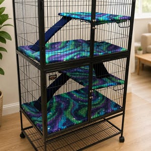May include: A tall, black metal multi-level animal cage featuring two main sections with double doors. The interior includes ramps and platforms covered in a fabric with a vibrant purple, blue, and green aurora borealis pattern.