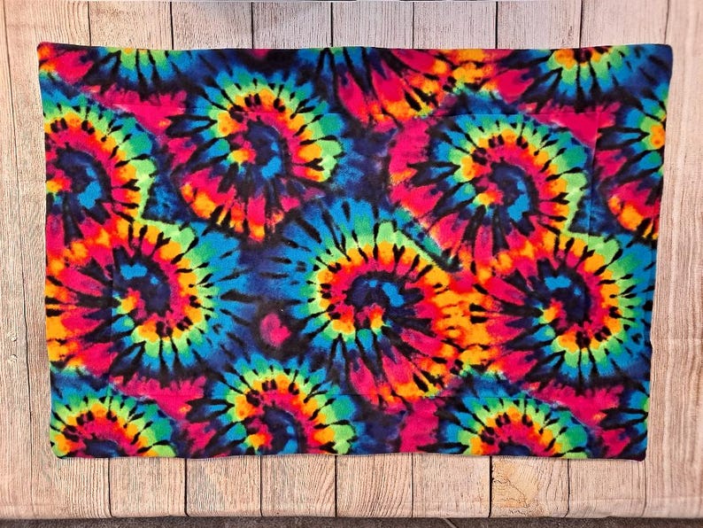 Może przedstawiać: Prostokątna poszewka na poduszkę z żywym wzorem tie-dye, przedstawiająca powtarzające się spiralne motywy w jasnych odcieniach neonowego r&oacute;żu, elektrycznego błękitu, słonecznego ż&oacute;łtego i limonkowego, na głębokim czarnym tle tkaniny.