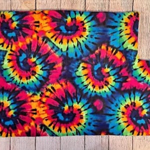 Może przedstawiać: Prostokątny kawałek materiału z żywym wzorem tie-dye z wirującymi spiralami w jasnych odcieniach neonowego r&oacute;żu, elektrycznego błękitu, limonki i ż&oacute;łci na ciemnym tle. Tkanina ma miękką, pluszową teksturę na całej swojej powierzchni.