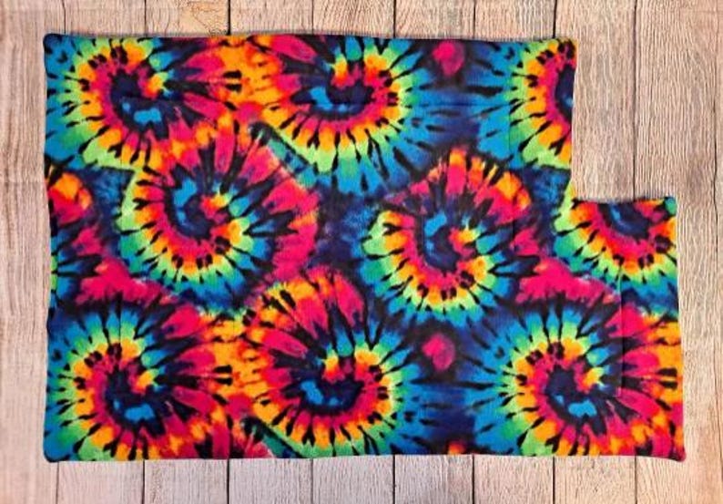 Może przedstawiać: Prostokątny kawałek materiału z żywym wzorem tie-dye z wirującymi spiralami w jasnych odcieniach neonowego r&oacute;żu, elektrycznego błękitu, limonki i ż&oacute;łci na ciemnym tle. Tkanina ma miękką, pluszową teksturę na całej swojej powierzchni.