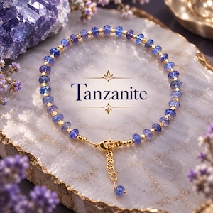 Può includere: Un braccialetto delicato con perline di tanzanite blu sfaccettate alternate a piccoli distanziatori metallici dorati. Il gioiello include una chiusura a moschettone dorata e una catenella di estensione regolabile con una singola perla di tanzanite. Il testo Tanzanite è centrato.