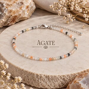 Puede incluir: Una delicada pulsera de cuentas con pequeñas piedras de ágata facetadas en tonos blanco translúcido, naranja suave y gris oscuro. La pulsera incluye un cierre de mosquetón de metal plateado y una cadena extensora ajustable.