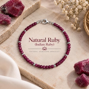 Peut inclure: Un bracelet de perles composé de petites pierres précieuses rubis facettées rouge foncé, alternées avec de minuscules perles métalliques argentées. Le bracelet possède un fermoir mousqueton argenté. Le texte indique : Natural Ruby (Indian Ruby) NATURAL GEMSTONE BRACELET.