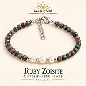 Op de afbeelding: Een armband met gefacetteerde robijn-zoisiet kralen in groen- en magentatinten, geaccentueerd door drie witte zoetwaterparels en kleine zilverkleurige metalen tussenstukjes. Het sieraad heeft een zilverkleurige karabijnsluiting en een verstelbare ketting.