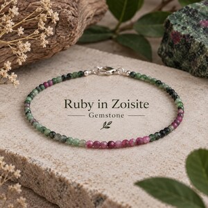 May include: A delicate bracelet composed of small, faceted ruby in zoisite gemstone beads in shades of green and magenta, secured with a silver-toned metal lobster clasp. The text Ruby in Zoisite Gemstone is printed in the center of the bracelet.