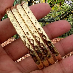 Pode incluir: Um conjunto de três pulseiras de metal dourado com uma textura martelada e uma série de marcas circulares reentrantes ao longo da superfície exterior. As pulseiras têm um acabamento polido e um perfil arredondado que reflete a luz.