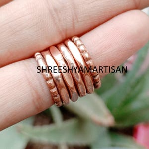 May include: A set of six copper-coloured rings stacked together. The outer rings feature a textured, notched pattern, while the four inner rings have a smooth, rounded surface. The text SHREESHYAMARTISAN is overlaid across the centre of the rings.