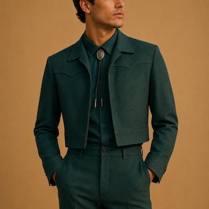 Puede incluir: Una chaqueta corta de color verde oscuro con un canesú puntiagudo de estilo western, mangas largas y dobladillo recto. La chaqueta se lleva sobre una camisa abotonada verde oscuro a juego con una corbata bolo plateada y un colgante circular.