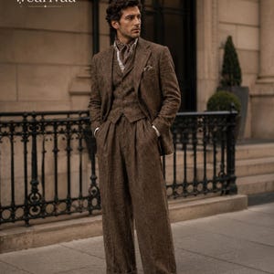 Puede incluir: Un traje de tres piezas de tweed marrón que incluye una chaqueta, un chaleco abotonado y pantalones anchos con dobladillo. El conjunto se completa con una camisa de cuello claro y un pañuelo estampado. El texto "W wearivaa" aparece arriba a la izquierda.