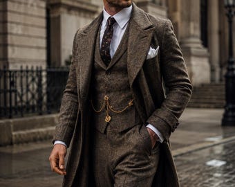 May include: A brown tweed three-piece suit consisting of a long overcoat, a waistcoat, and trousers, worn with a white collared shirt, a dark patterned tie, and a gold pocket watch chain. The text wearivaa TIMELESS STYLE. MODERN CONFIDENCE. is visible.