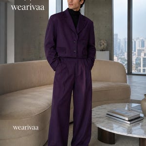 Puede incluir: Un traje de dos piezas de color morado intenso que consta de una chaqueta corta con solapa de muesca y dos botones, combinada con pantalones de pernera ancha y cintura alta. El texto "W wearivaa" aparece arriba a la izquierda.