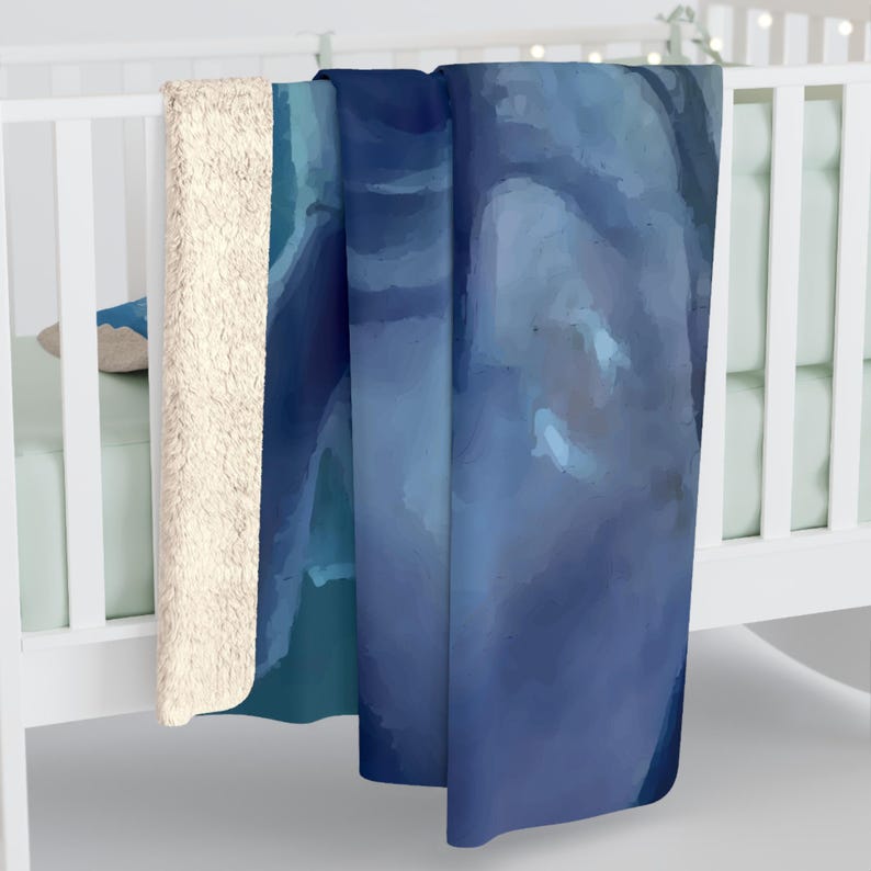 May include: A plush sherpa-lined throw blanket featuring a smooth, abstract watercolour print in various shades of deep navy, royal blue, and light sky blue. The blanket has a thick, textured cream-coloured fleece backing visible along the folded edge.